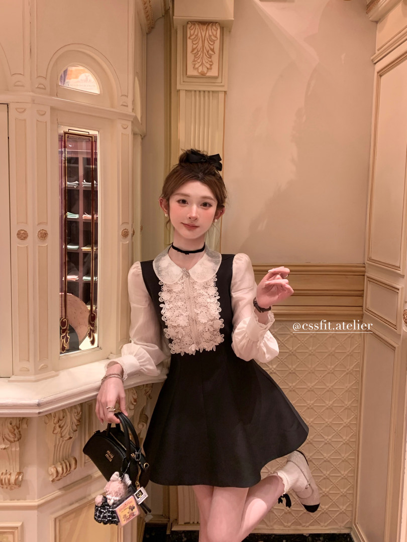 Model wearing a black dress with white lace blouse details and a small black handbag