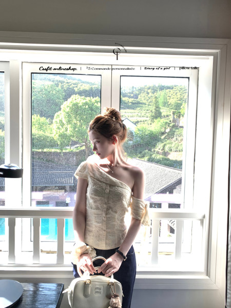 Woman modeling a light one-shoulder lace top with a small handbag indoors