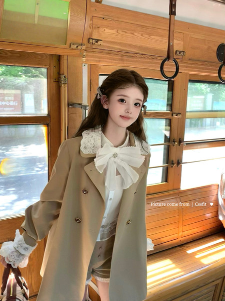 Model wearing a beige trench-style coat with a white lace blouse and oversized bow