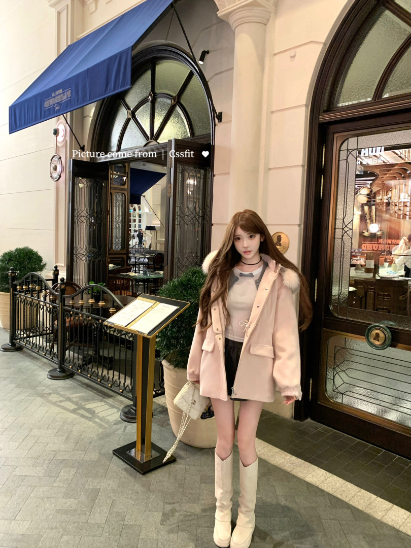 Woman wearing a pale pink winter coat with boots and a small handbag