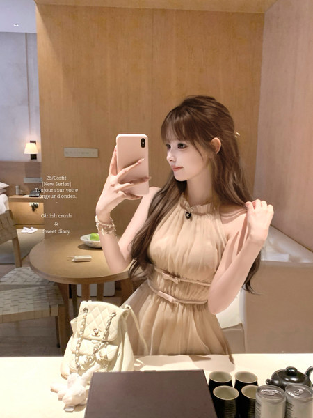Woman wearing a beige sleeveless dress with a quilted chain handbag in a mirror selfie