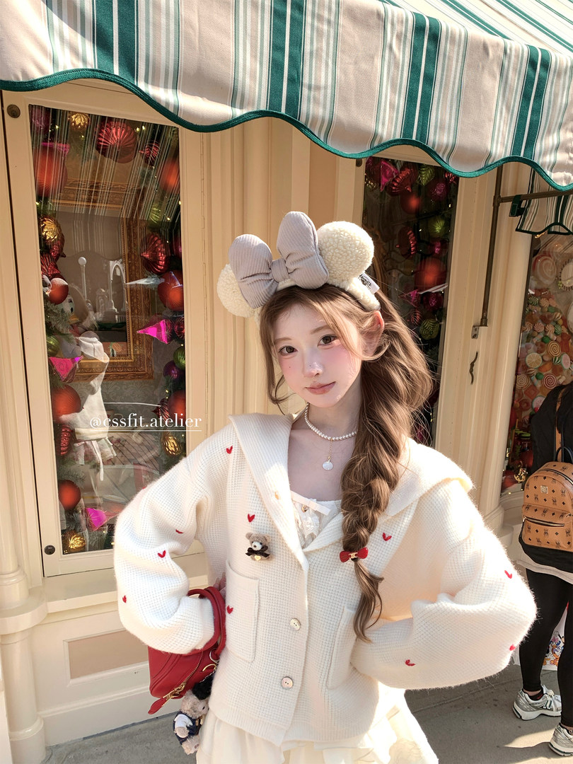 Woman modeling a white heart-embroidered cardigan with a matching bow earmuff headband