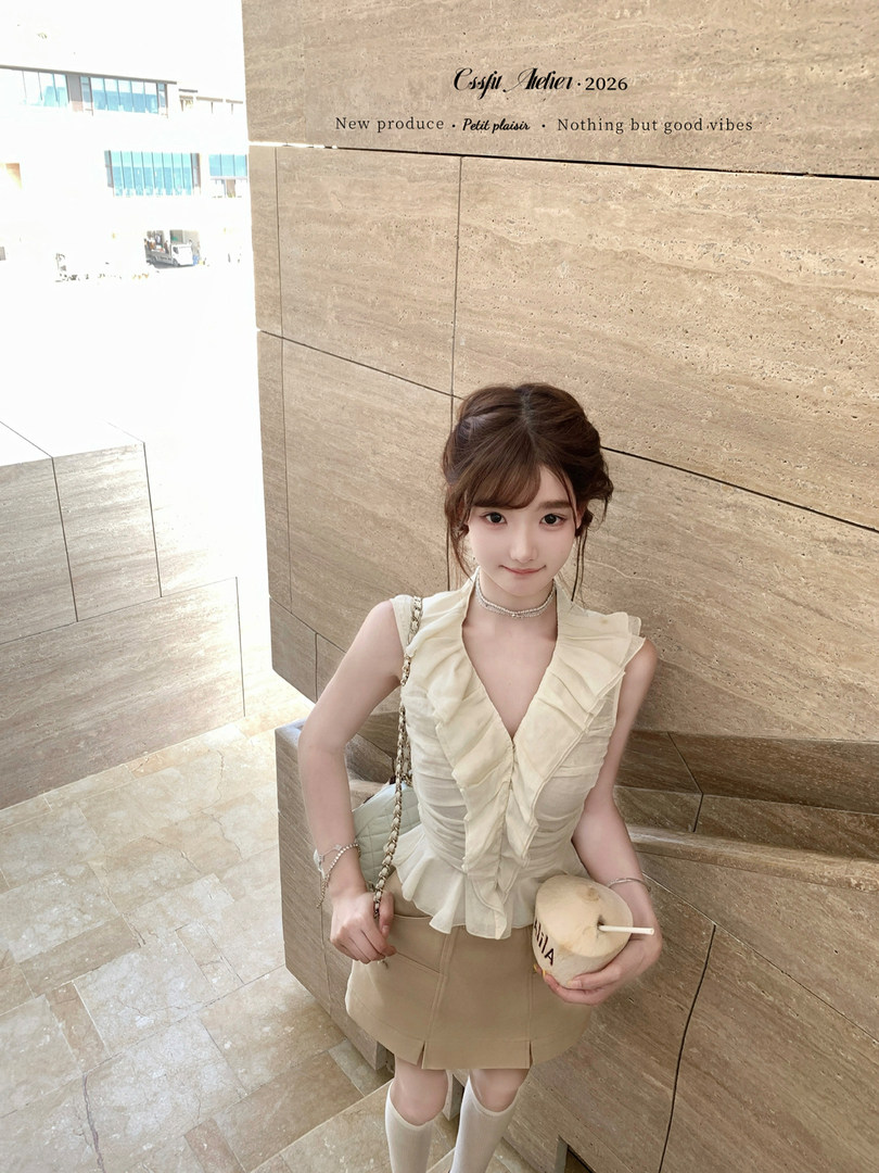 Woman modeling a cream ruffled sleeveless top with a beige mini skirt