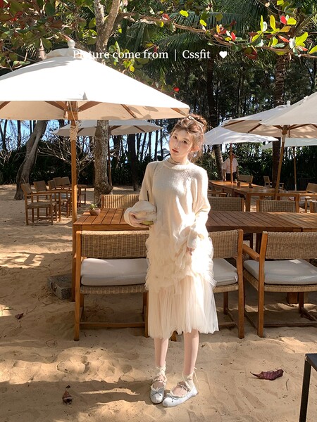 Woman wearing a cream layered dress and sweater at a beachside cafe