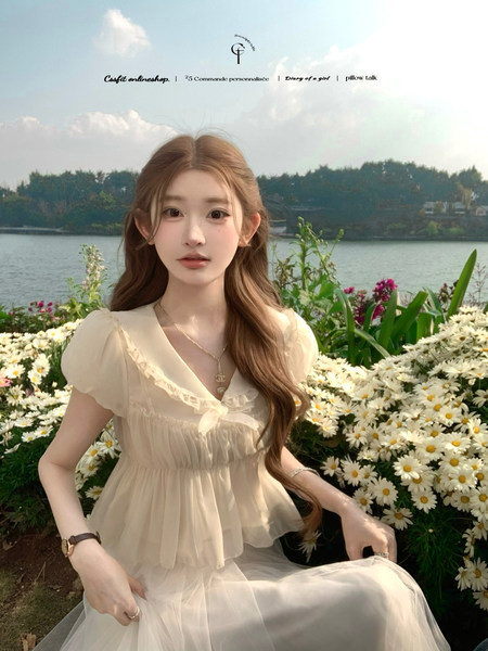 Woman wearing a light cream sheer ruffled dress outdoors by the water and flowers