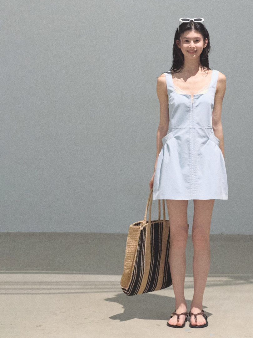 Woman wearing a light blue sleeveless mini dress with a striped tote bag