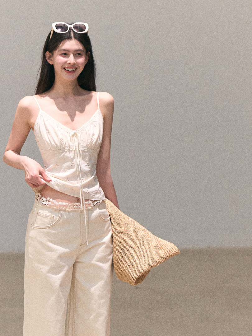 Model wearing a cream camisole top and wide-leg pants with a woven tote bag
