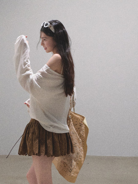 Woman wearing an off-shoulder white top with a brown skirt and tan bag