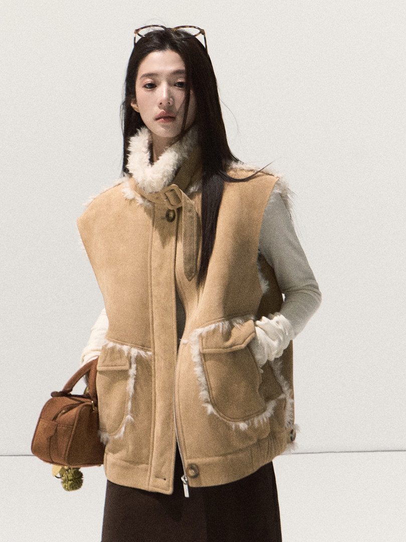 Model wearing a beige shearling-lined vest with a brown handbag