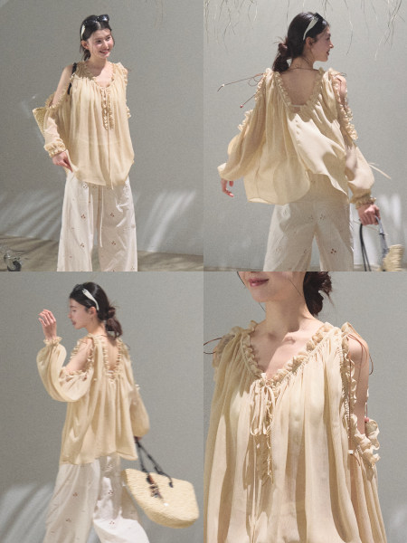 Model wearing a light beige sheer ruffled blouse with white pants