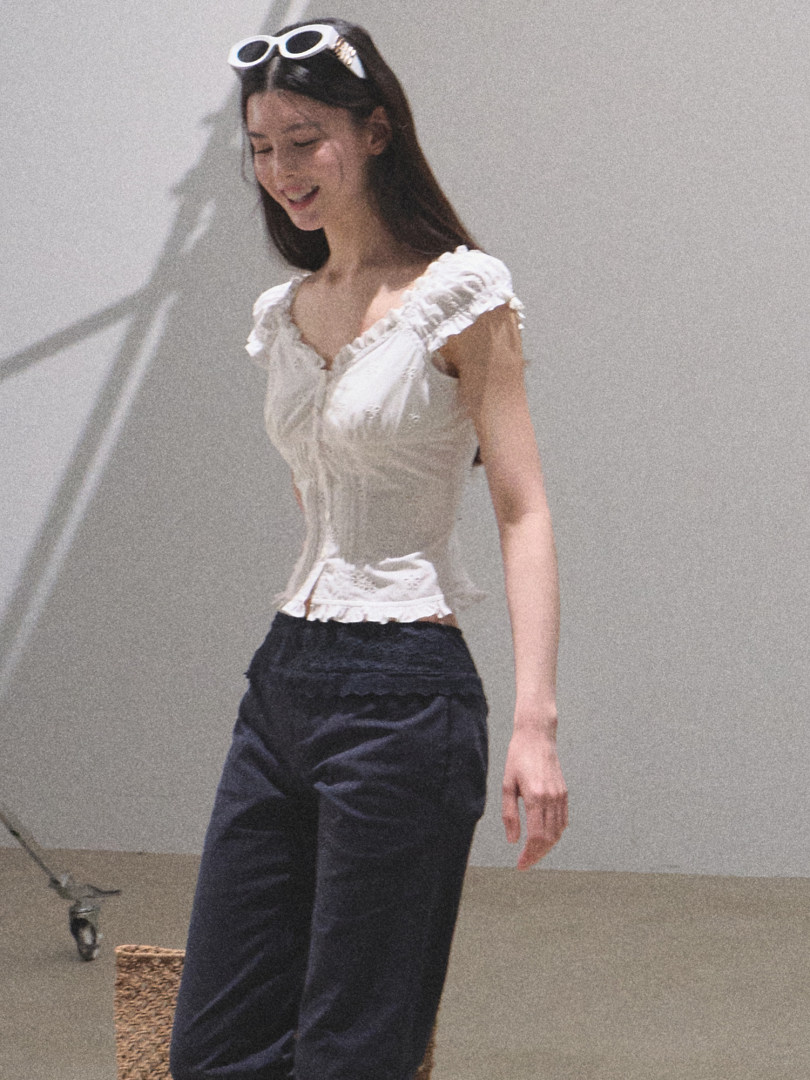 Model wearing a white ruffled sleeveless top with dark pants