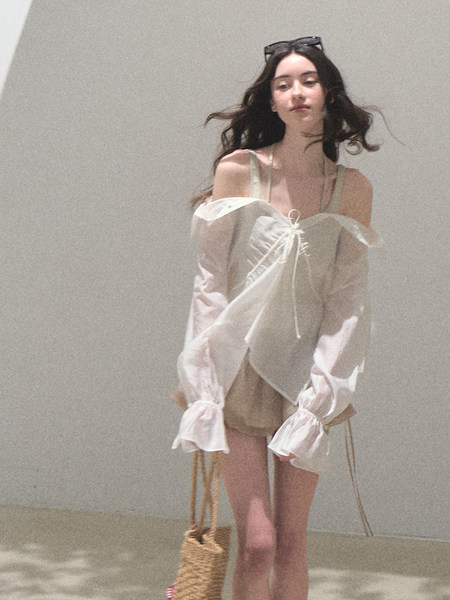 Model wearing a sheer off-shoulder long-sleeve blouse with a tie front