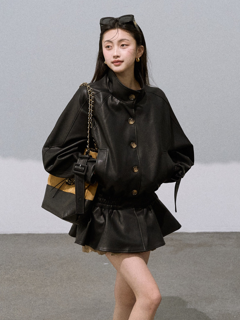 Model wearing a black leather jacket and matching mini skirt with a chain-strap bag