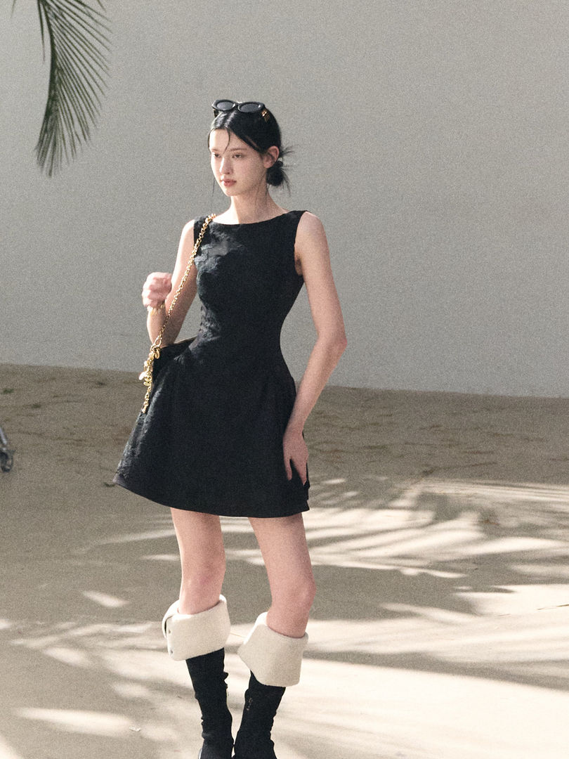 Model wearing a black sleeveless mini dress with boots and a chain bag