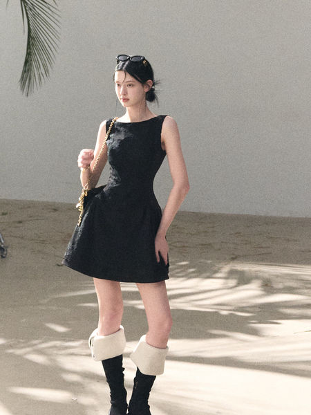 Model wearing a black sleeveless mini dress with boots and a chain bag
