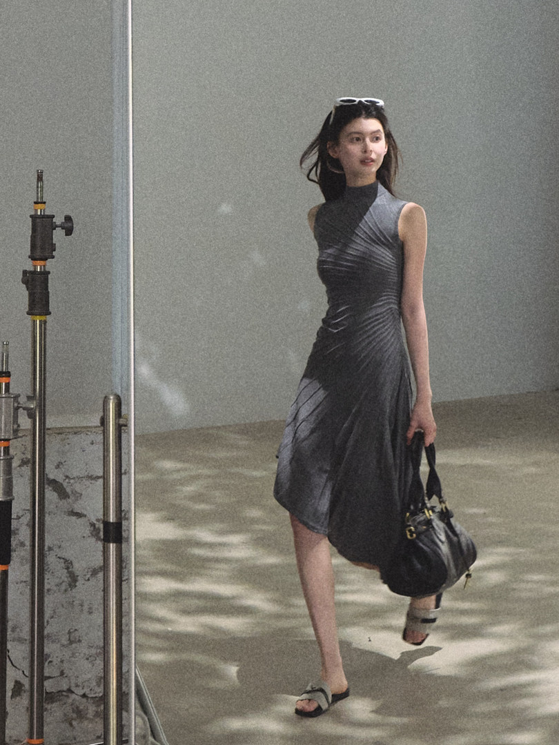 Model wearing a dark draped sleeveless dress and carrying a black handbag