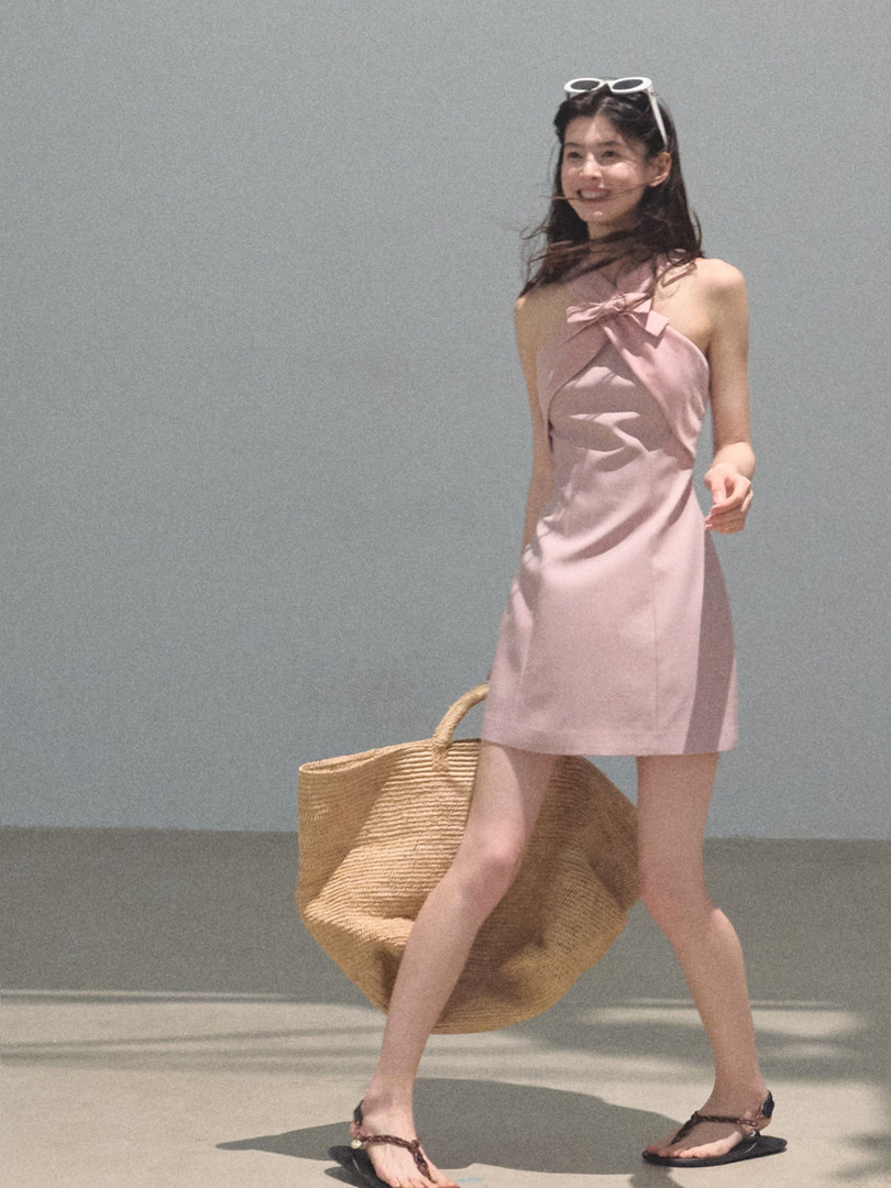 Woman wearing a pink halter mini dress with a large woven tote bag