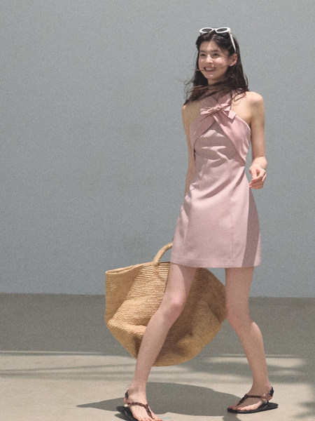 Woman wearing a pink halter mini dress with a large woven tote bag