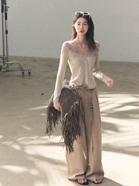 Woman modeling a beige lace-trimmed long-sleeve top with wide-leg pants and a fringed clutch