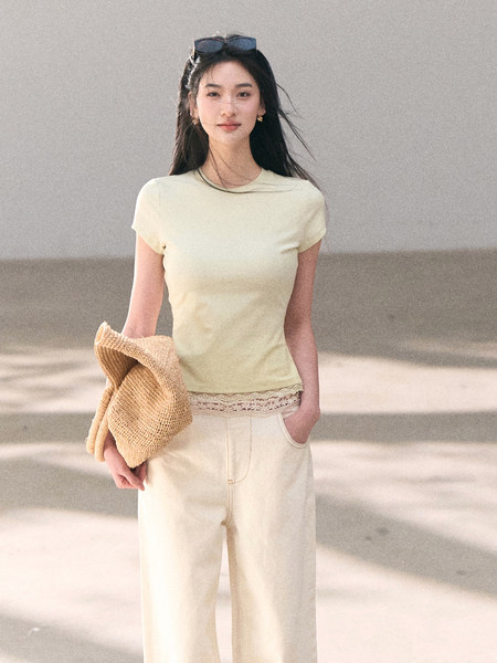 Model wearing a light yellow short-sleeve top and cream wide-leg pants holding a straw hat