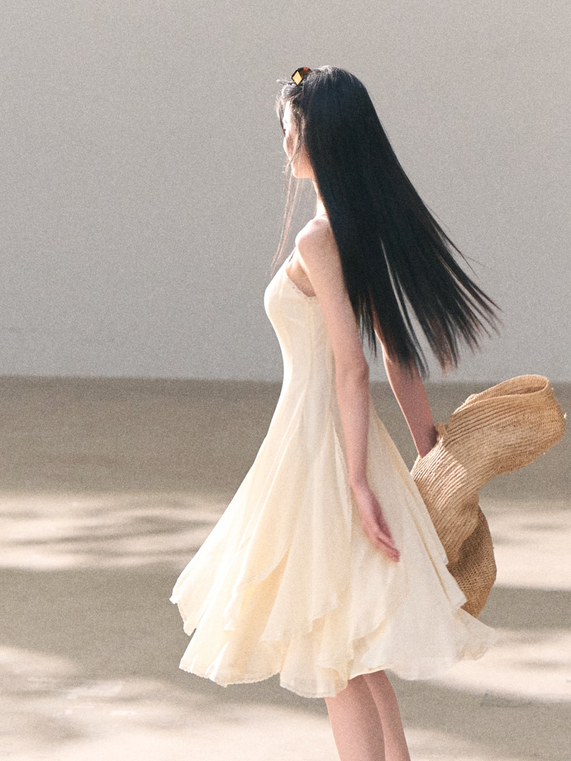 Woman wearing a cream sleeveless dress holding a woven straw bag
