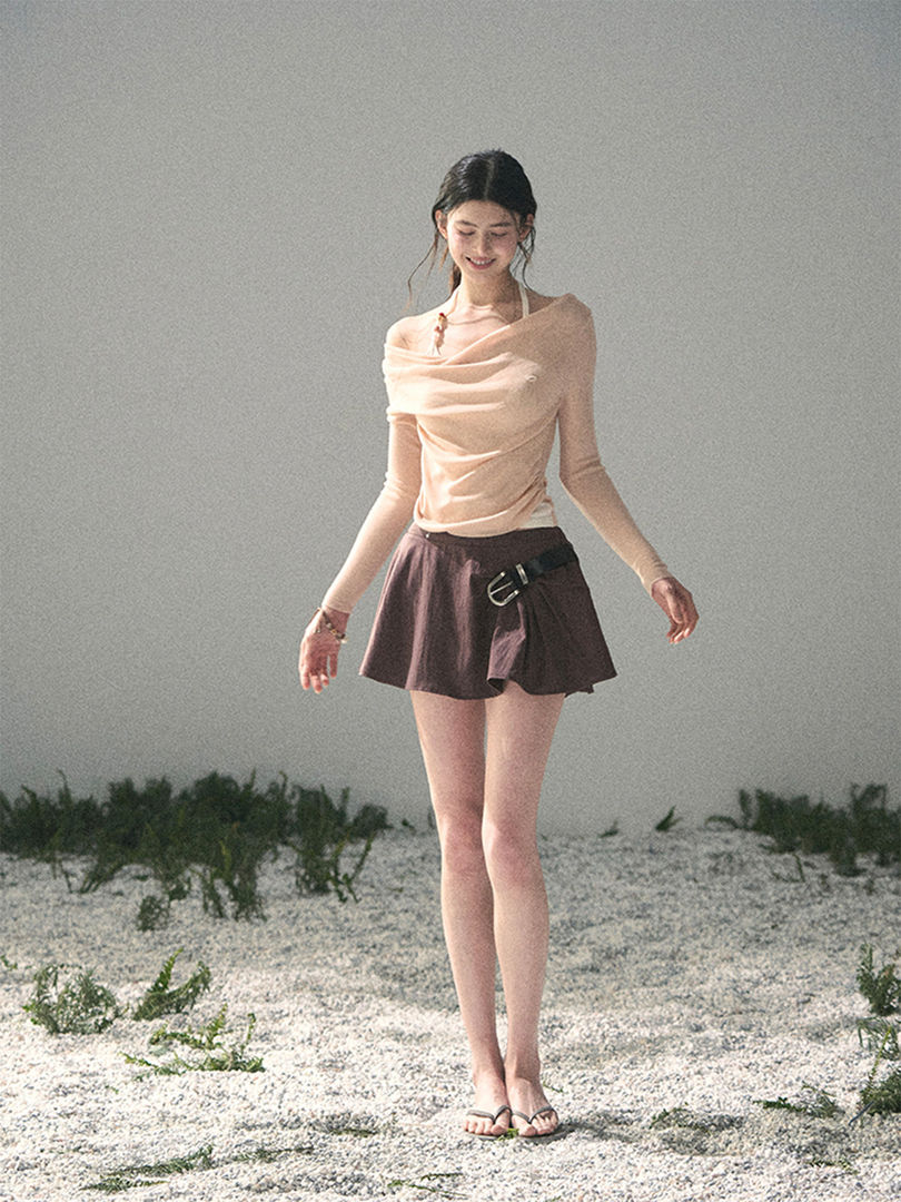 Model wearing a sheer off-shoulder top with a short skirt on a beach