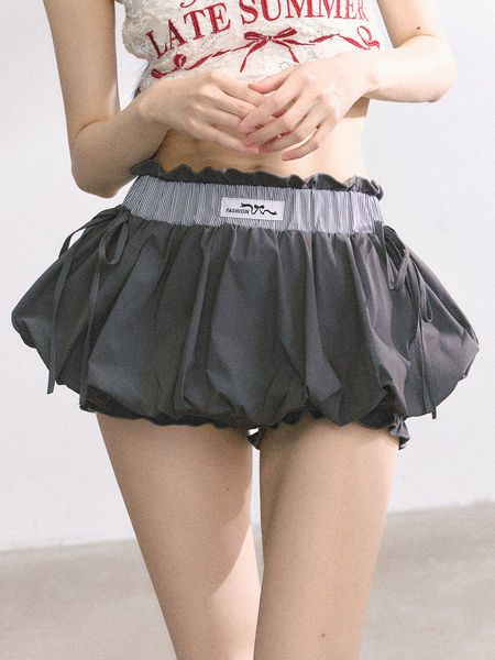 Model wearing dark ruffled bloomer shorts with a striped elastic waistband