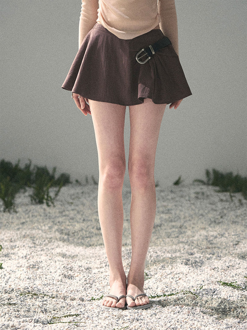 Model wearing a dark pleated mini skirt with belt detail and sandals