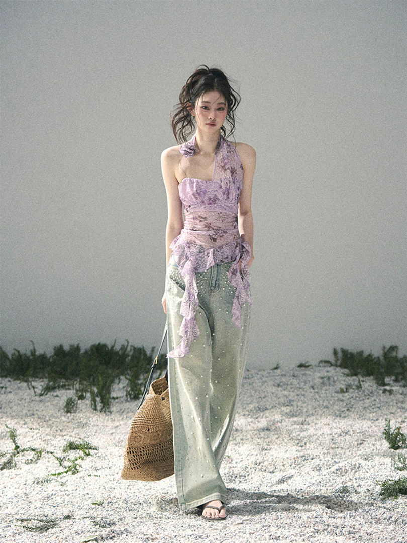 Model wearing a pastel halter top with wide-leg pants and a woven tote on a beach