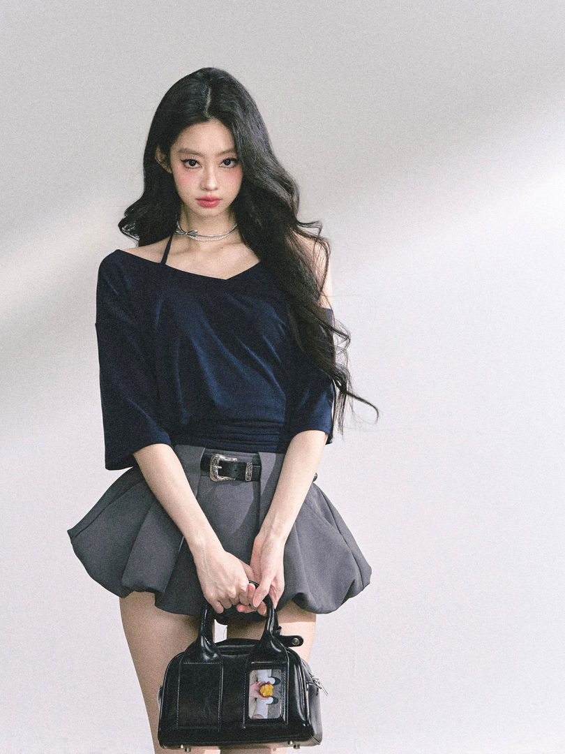 Fashion model wearing a black off-shoulder top with a gray mini skirt and holding a black handbag