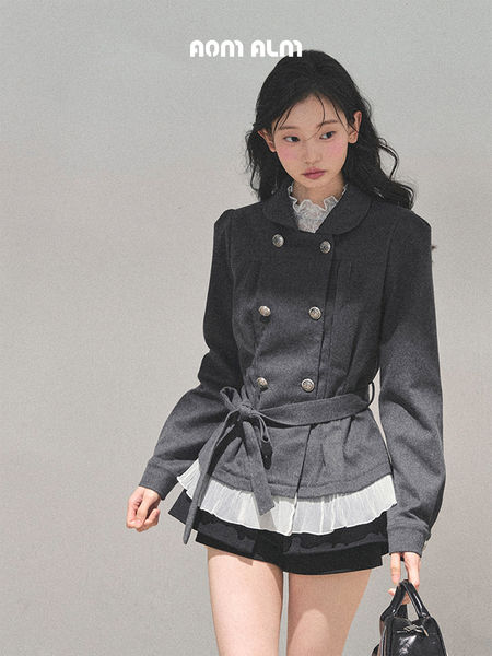 Model wearing a dark gray belted double-breasted jacket with a layered white blouse and black shorts