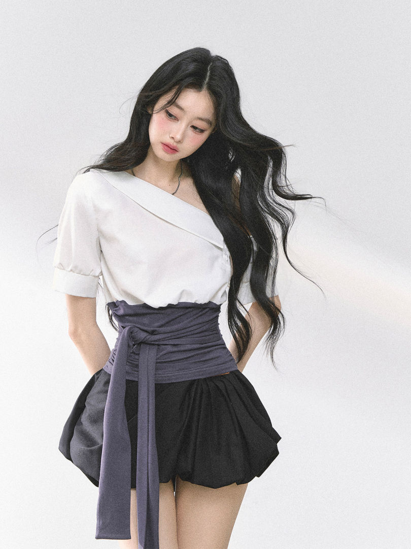 Model wearing a white off-shoulder top with a purple waist wrap and black skirted shorts