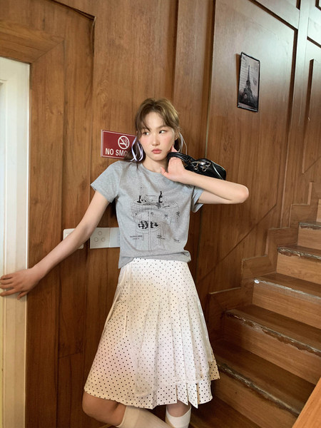 Model wearing a gray graphic T-shirt and white polka dot pleated skirt