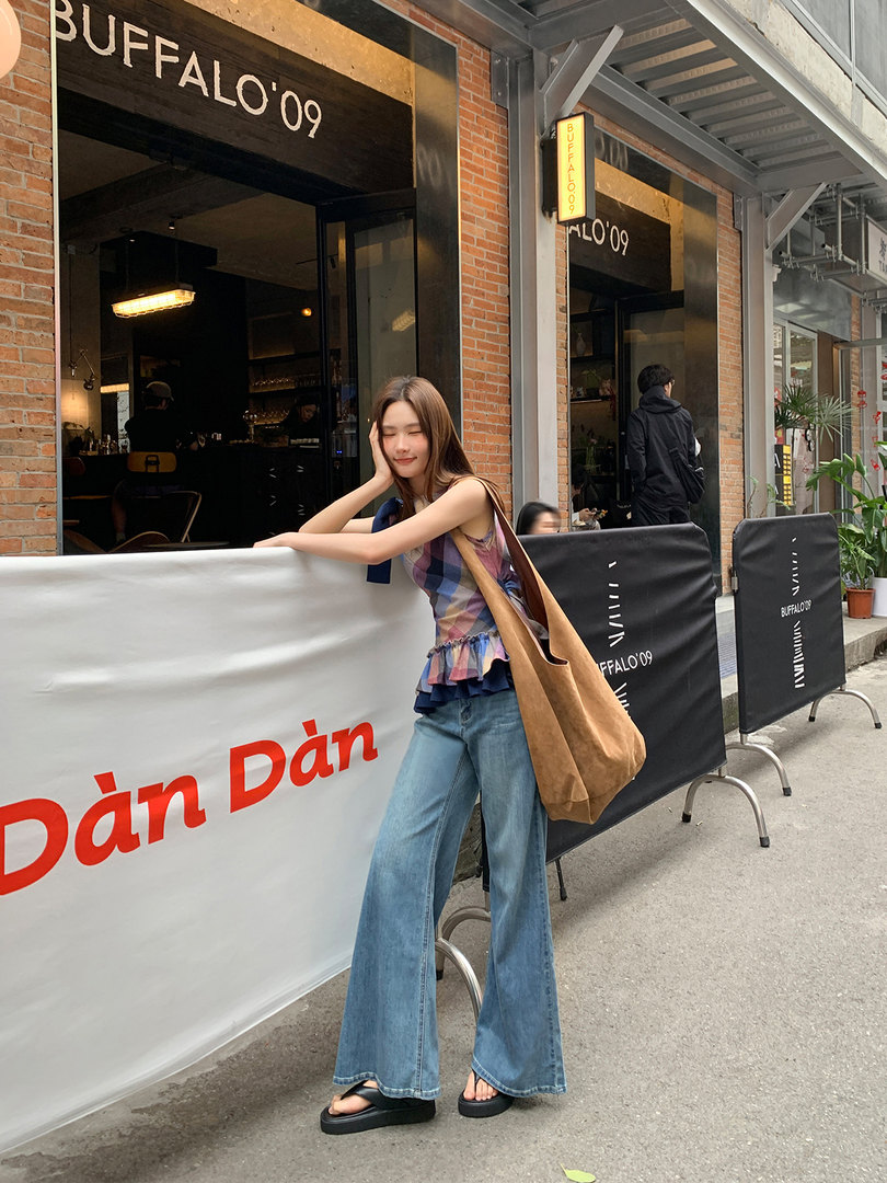 Woman wearing a plaid sleeveless top, flared jeans, and platform sandals outdoors