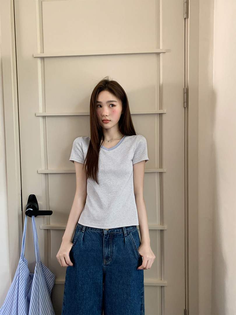 Young woman wearing a light gray short-sleeve fitted top with blue jeans