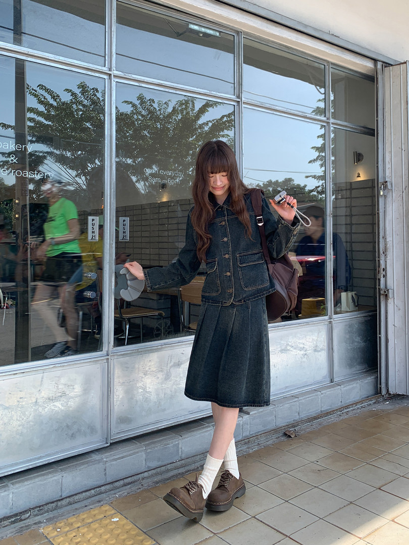 Woman wearing a dark denim jacket and matching skirt with brown shoes outdoors