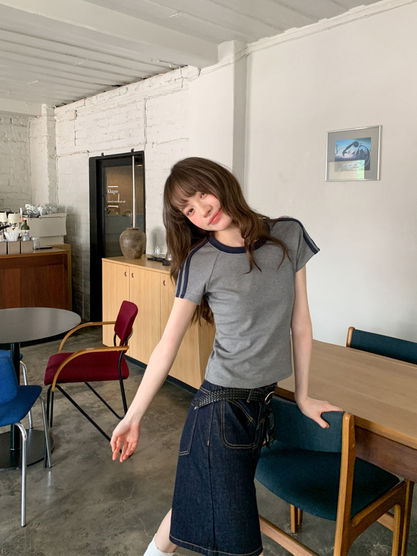 Woman wearing a gray fitted short-sleeve top with a denim skirt in a cafe