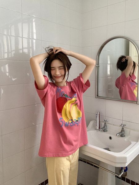 Model wearing a pink graphic oversized T-shirt with light pants in a bathroom
