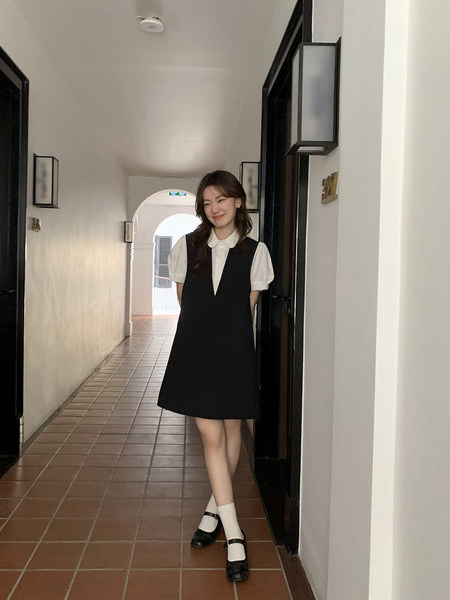 Model wearing a black pinafore dress over a white puff-sleeve blouse
