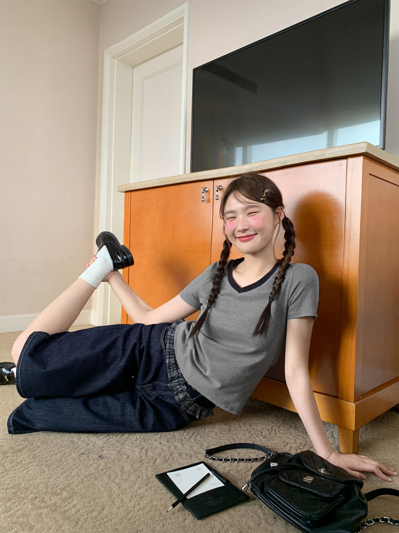 Young woman wearing a gray fitted T-shirt and dark wide-leg jeans while posing indoors