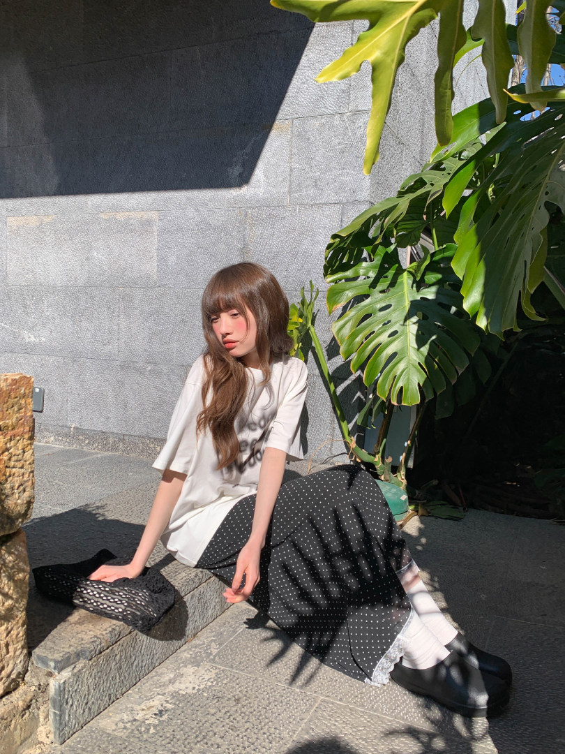 Model wearing a white oversized T-shirt with a black polka dot skirt and black shoes outdoors