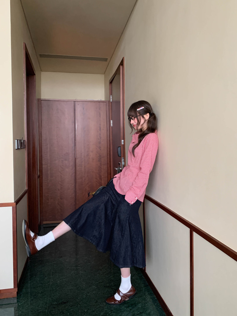 Woman wearing a pink checkered long-sleeve top with a dark skirt and Mary Jane shoes
