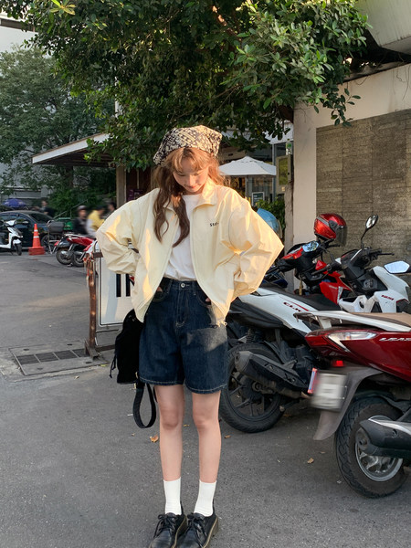 Woman wearing a cream lightweight jacket with denim shorts and sneakers