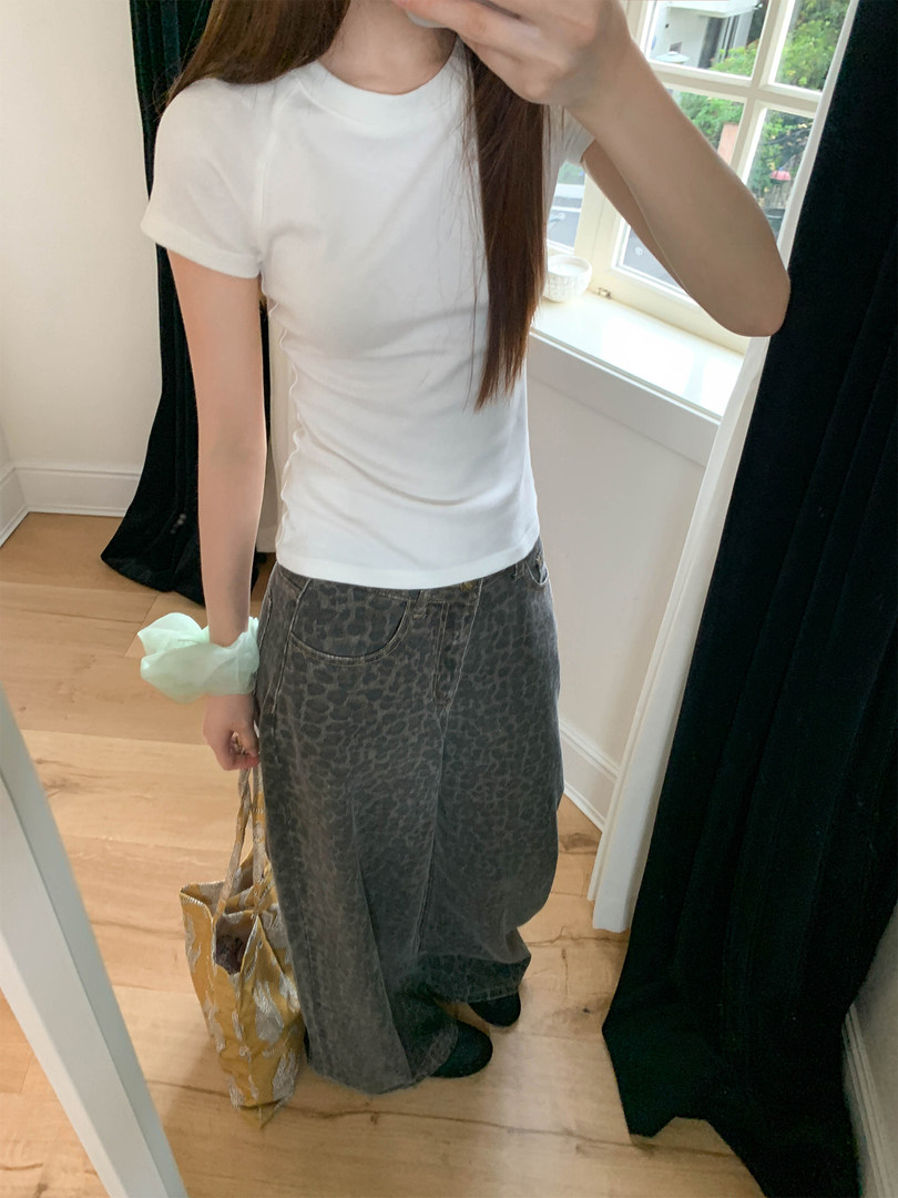 Mirror selfie of a model wearing a white fitted T-shirt and dark wide-leg patterned pants
