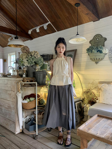 Model wearing a cream sleeveless halter top with a gray maxi skirt in a rustic interior