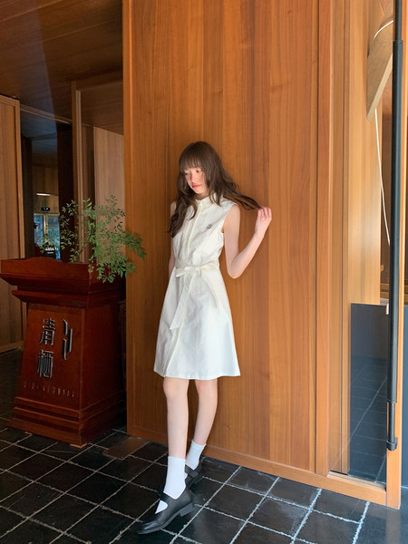 Woman wearing a white sleeveless belted dress with black shoes indoors