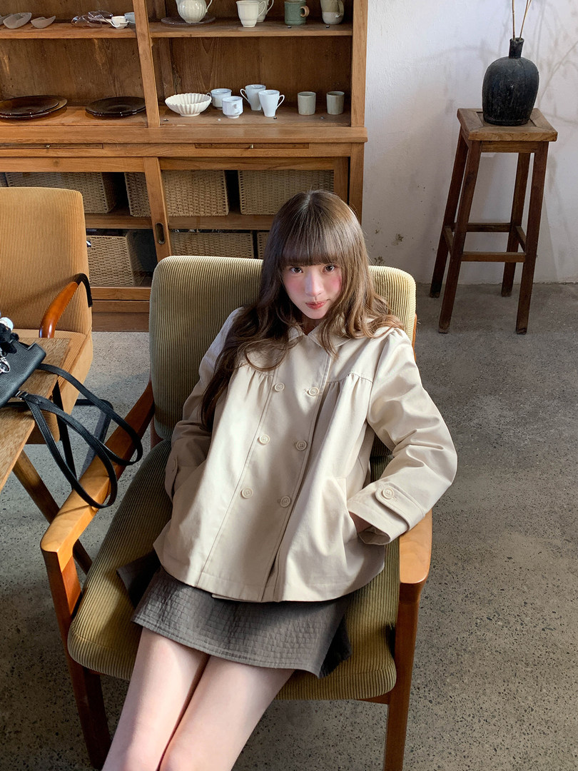 Woman wearing a beige double-breasted jacket with a gray skirt