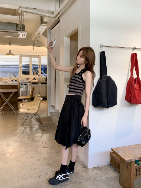 Woman wearing a striped sleeveless top and black skirt posing with a handbag