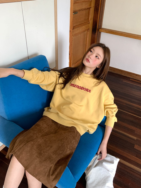 Woman wearing a yellow graphic sweatshirt with a brown skirt while sitting on a blue sofa