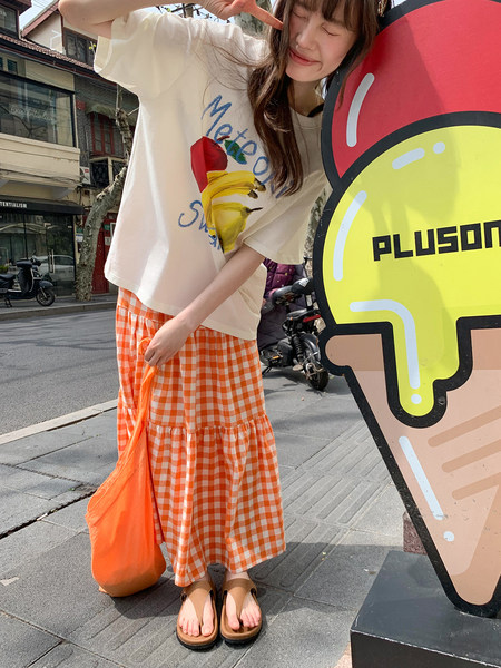 Model wearing an oversized graphic T-shirt with an orange gingham skirt and sandals outdoors